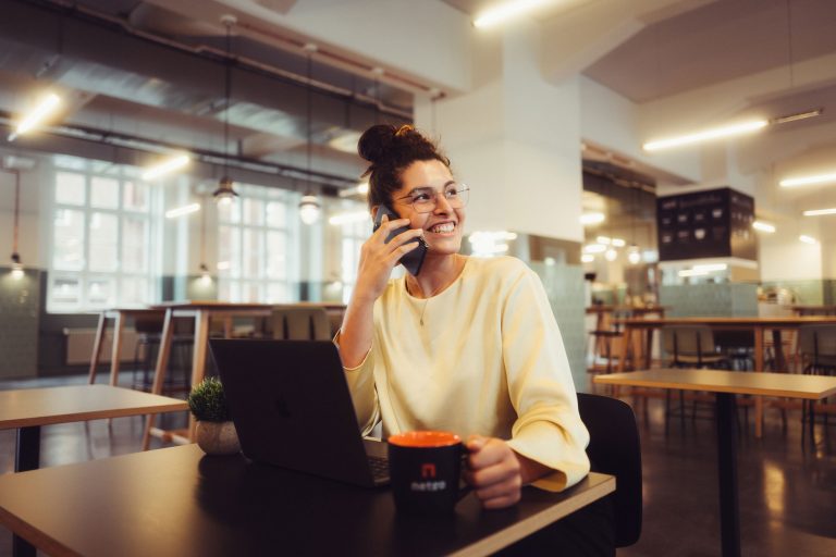 Frau sitzt in einem Café vor einem Laptop und telefoniert